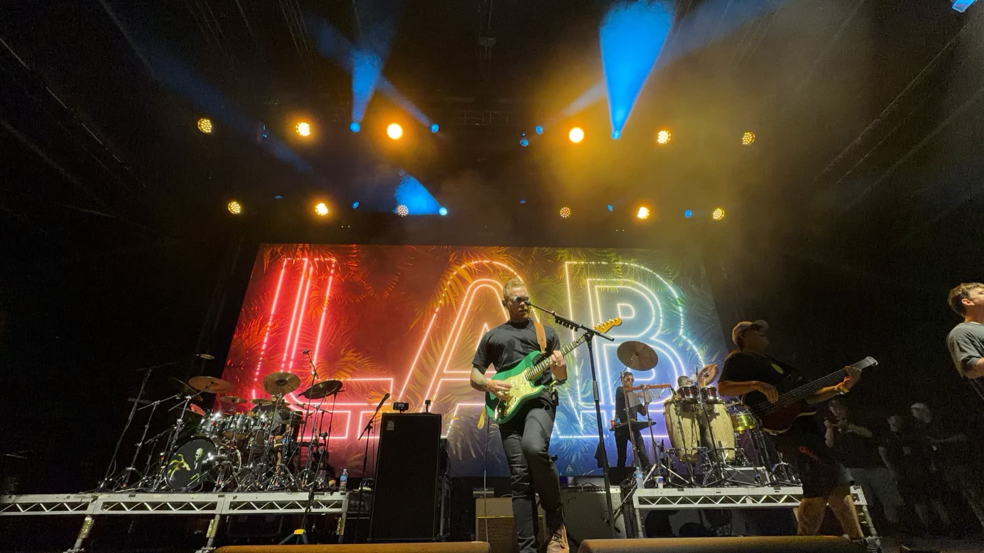 A band on stage under amber and blue lights with a neon backdrop