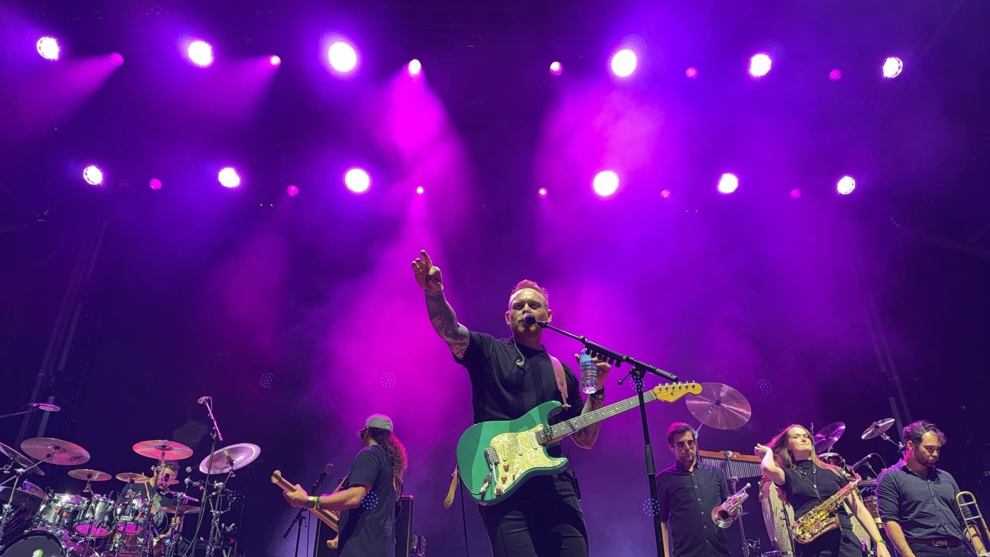 A guitarist pointing to the crowd under violet stage lights