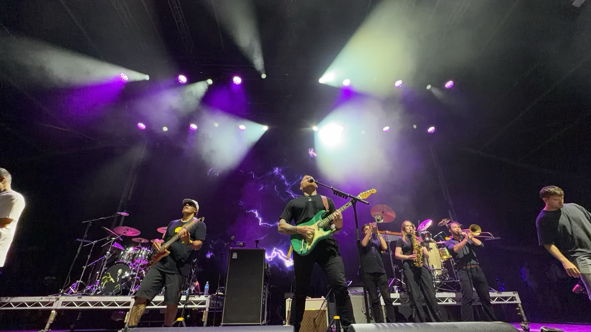 A band and horn section under purple and white spotlights