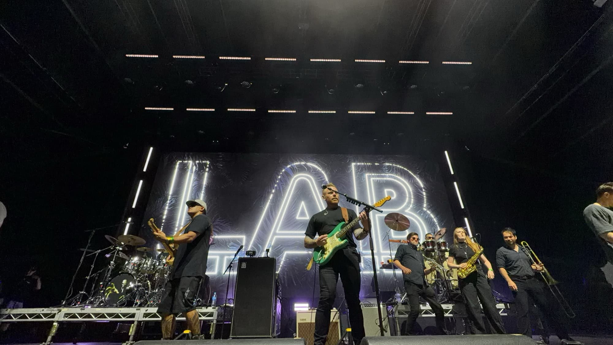 A band with a horn section on a dark stage under white light bars