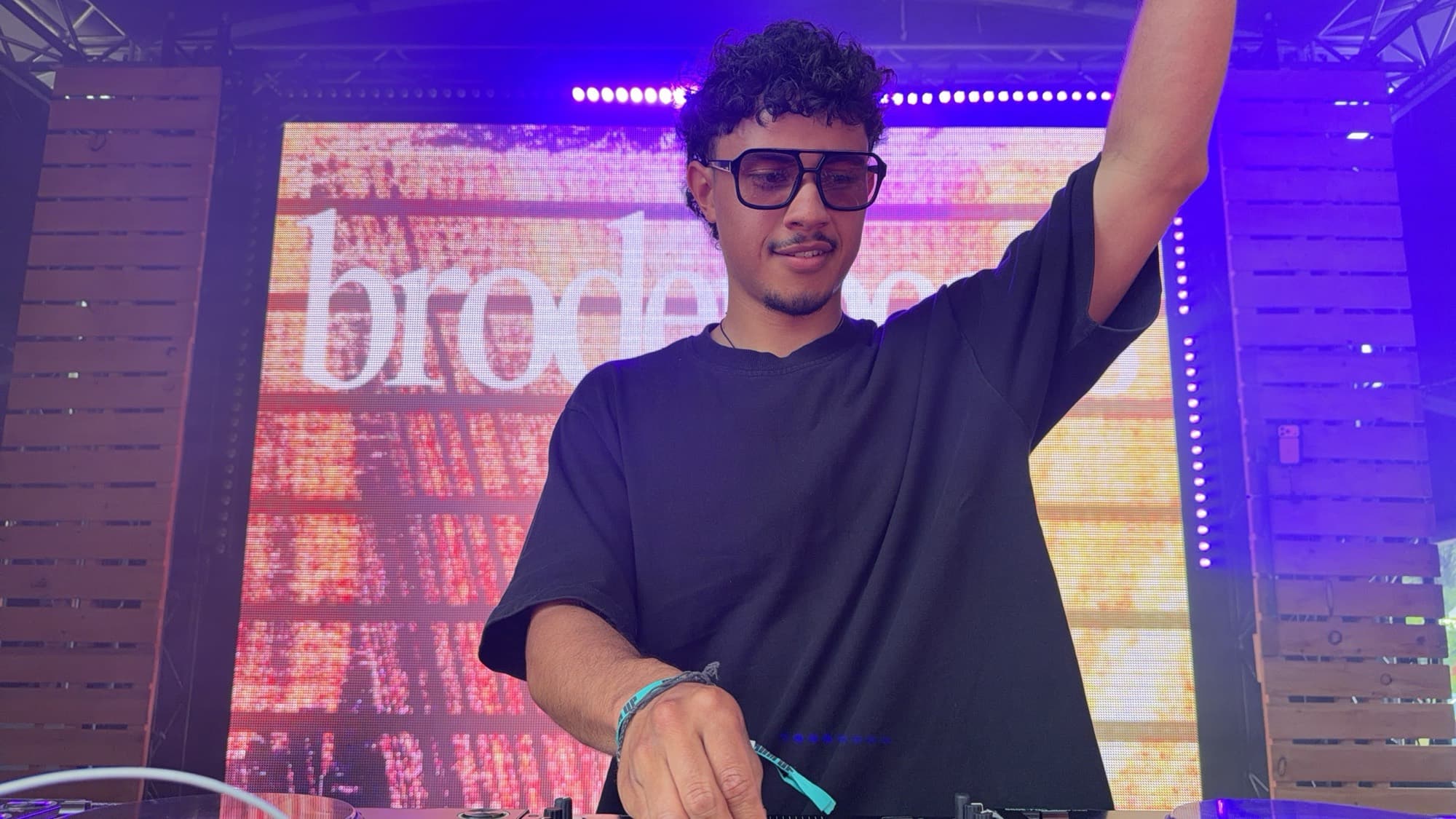 A DJ with one hand in the air in front of a glowing LED wall